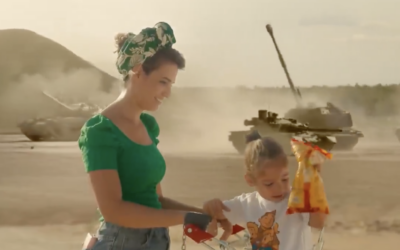 A still image from the now-removed music video for the song 'Notnim Yadayim' ('Lending Hands'), which was included in the IDF Rabbinate's 2026 Passover Haggadah, portrays a reservist's wife buying groceries wither her child as tanks stand in the background. (IDF Rabbinate)